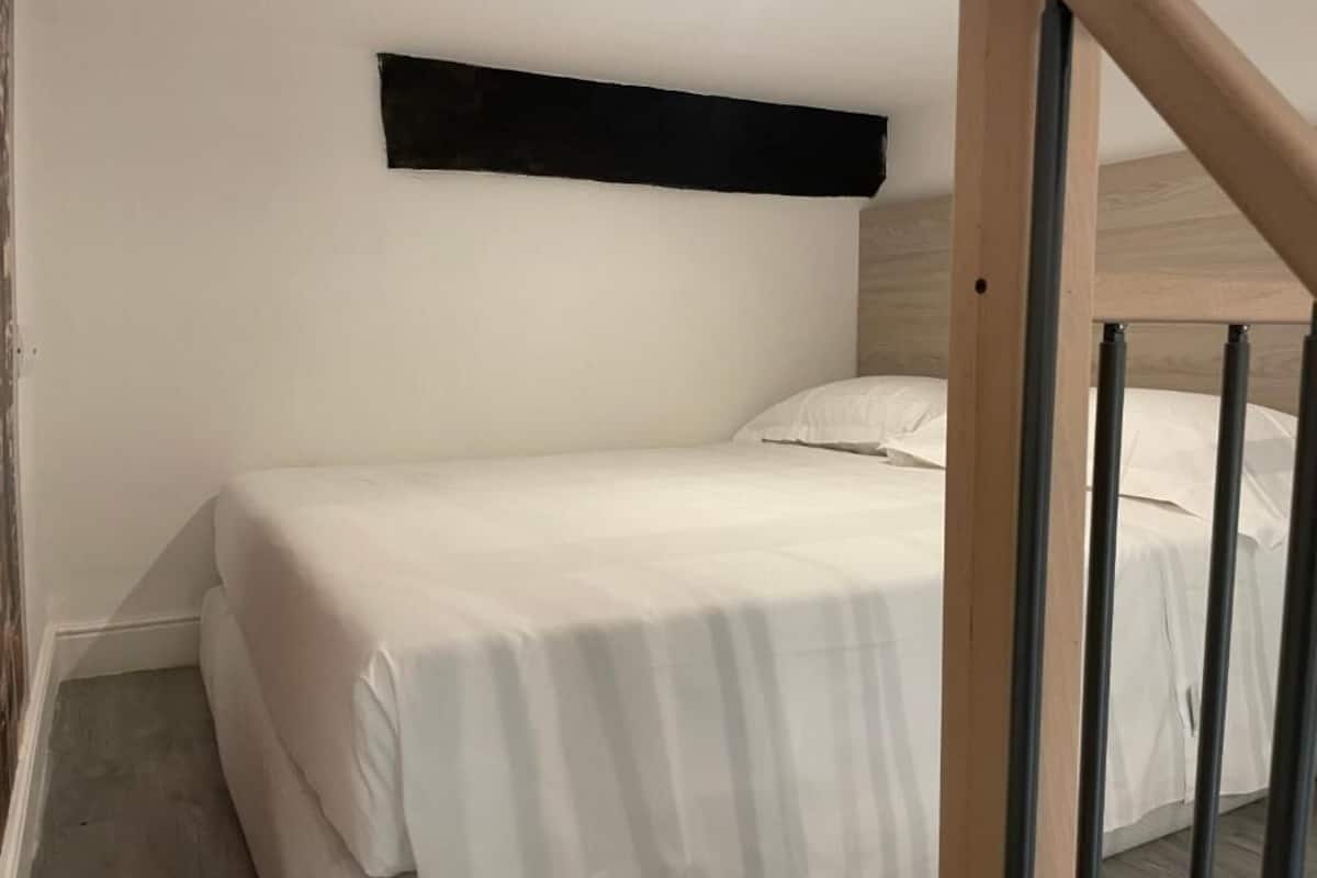 A single bed with white bedding in a room with white walls and a wooden headboard.