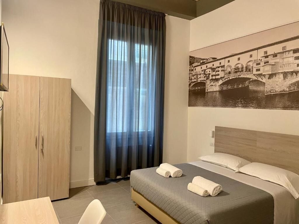 Una habitación de hotel con cama, armario, escritorio y un ventanal con cortinas.