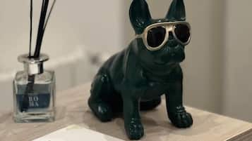 Eine dunkelgrüne Bulldogge-Figur mit Sonnenbrille auf einer Holztischplatte, zusammen mit einem Lufterfrischer und einer Visitenkarte.