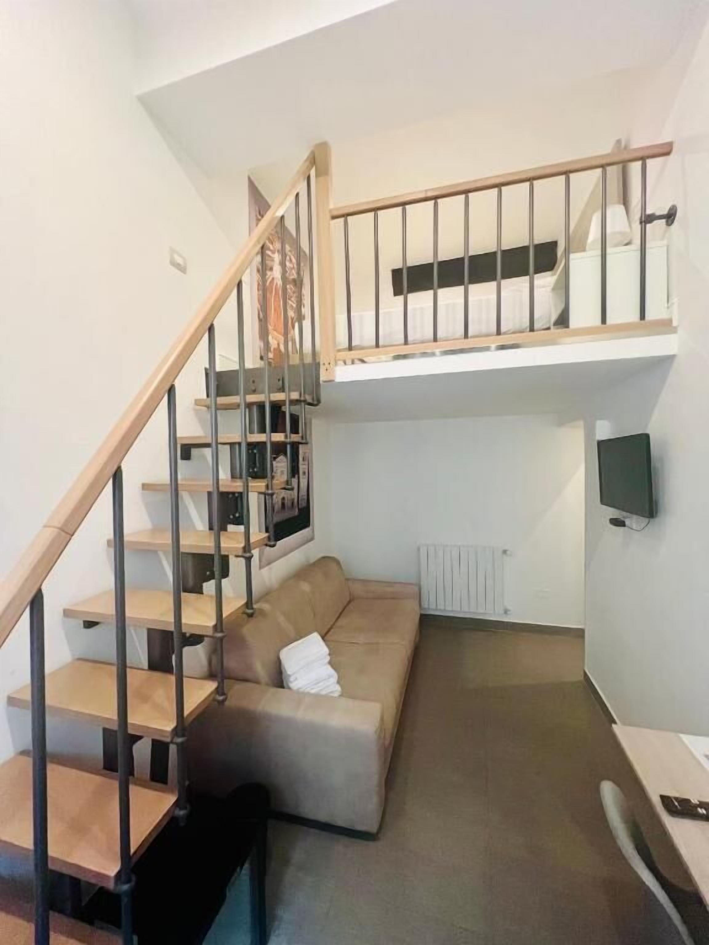 A modern loft-style room with a wooden staircase, a built-in sofa, a flat-screen TV, and a radiator.