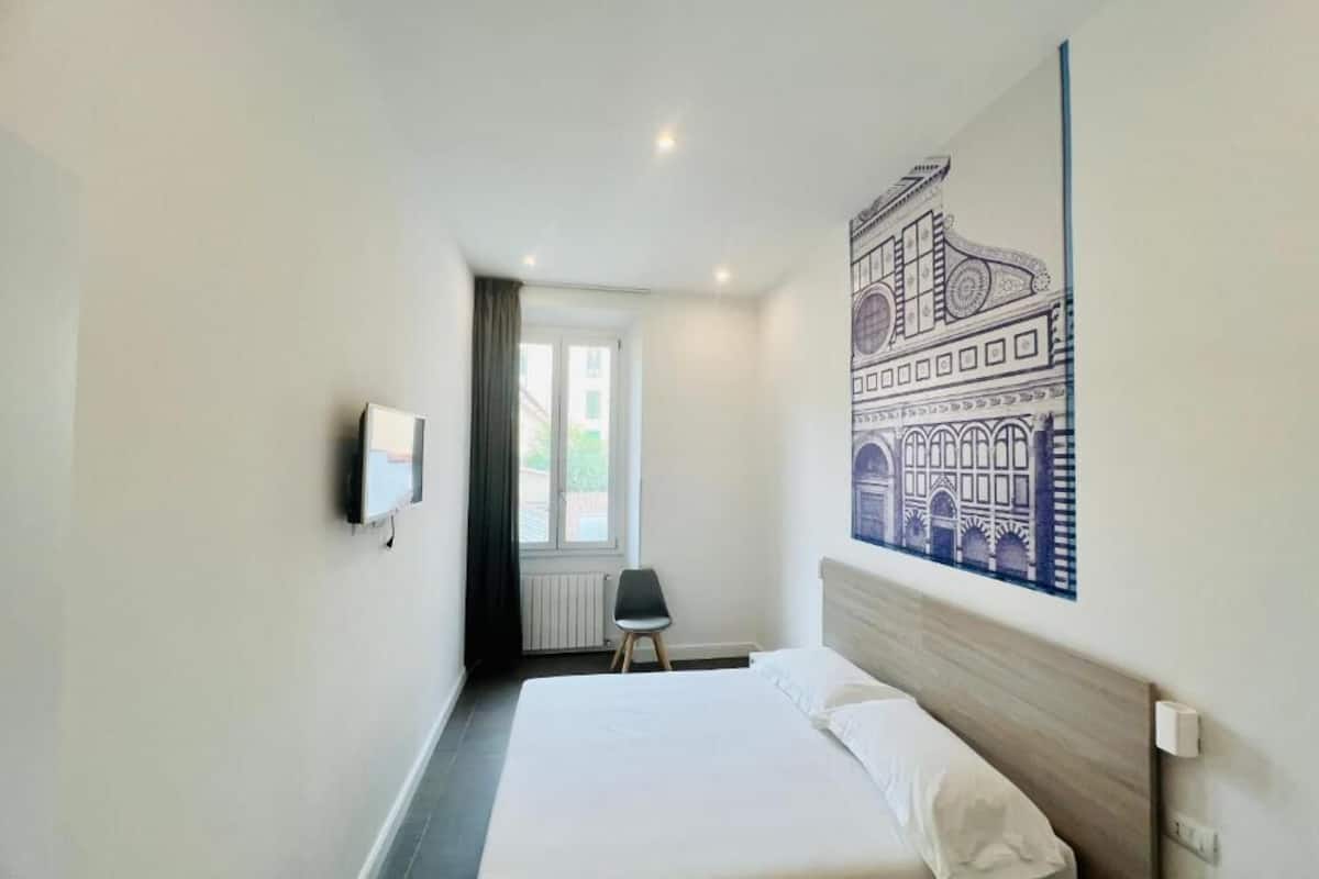 A hotel room with a bed, a television, a chair, and a large wall art piece.
