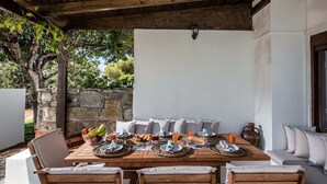 Ein Essbereich im Freien mit einem Holztisch, gedeckt für ein Frühstück, umgeben von Sitzgelegenheiten mit Kissen.