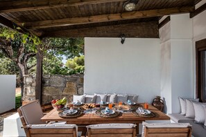 Ein Essbereich im Freien mit einem Holztisch, gedeckt für ein Frühstück, umgeben von Sitzgelegenheiten mit Kissen.