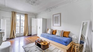 A bedroom with a bed, a bedside table, a mirror, and a window with curtains.