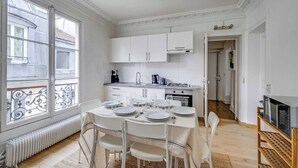 A modern kitchen with white cabinets, a dining table set for four, and a view through large windows.