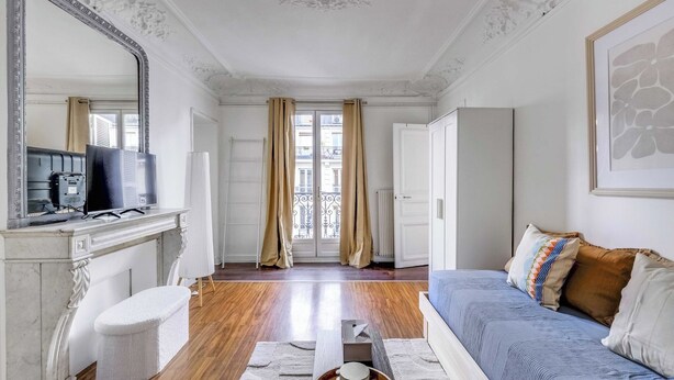 A room with a bed, a desk with a computer, a mirror, and a window with curtains.