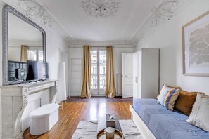 Una habitación con cama, escritorio con computadora, espejo y ventana con cortinas.