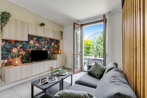 Ein modernes Wohnzimmer mit Fernseher, einer Couch, einem Couchtisch und einem Balkon mit Blick auf die Berge.