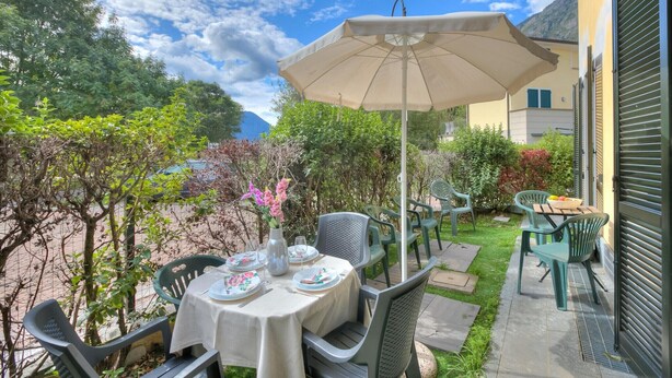 An outdoor patio with a table set for dining, surrounded by chairs and a large umbrella. - Mobilehome in Porlezza am Luganersee (Porlezza)