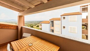 Un balcón con mesa y sillas de madera, con vistas a una zona residencial con edificios y un paisaje lejano.
