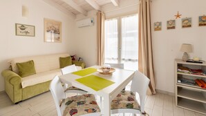 Una sala de estar acogedora con un sofá verde, una mesa blanca con individuales verdes y una estantería con diversos objetos.