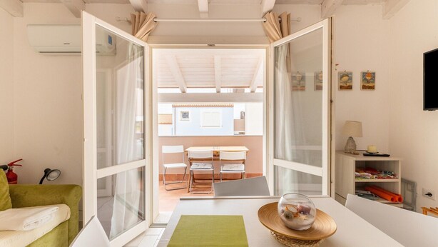 Habitación con una mesa de comedor, sillas, un sofá, un televisor y vistas al balcón a través de una puerta de cristal.