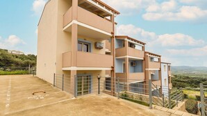 Un edificio residencial de varios pisos con balcones, un estacionamiento y vistas al campo.