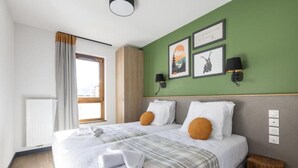 Una cama doble con sábanas blancas, dos almohadas y una manta de cuadros. Hay dos lámparas fijadas a la pared y tres cuadros enmarcados.
