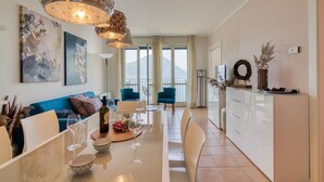 A modern living room with a blue sofa, dining table, and kitchen area. - Appartement mit Seeblick auf den Luganersee (Porlezza)