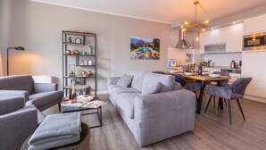 A modern living room with a grey sofa, a coffee table, and a dining area with a wooden table and chairs. - Appartement mit Seeblick auf den Luganersee (Porlezza)