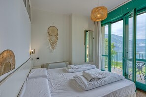 A hotel room with a bed, a dreamcatcher, a hanging light, and a balcony with a view of the mountains. - Appartement mit Seeblick auf den Luganersee (Porlezza)