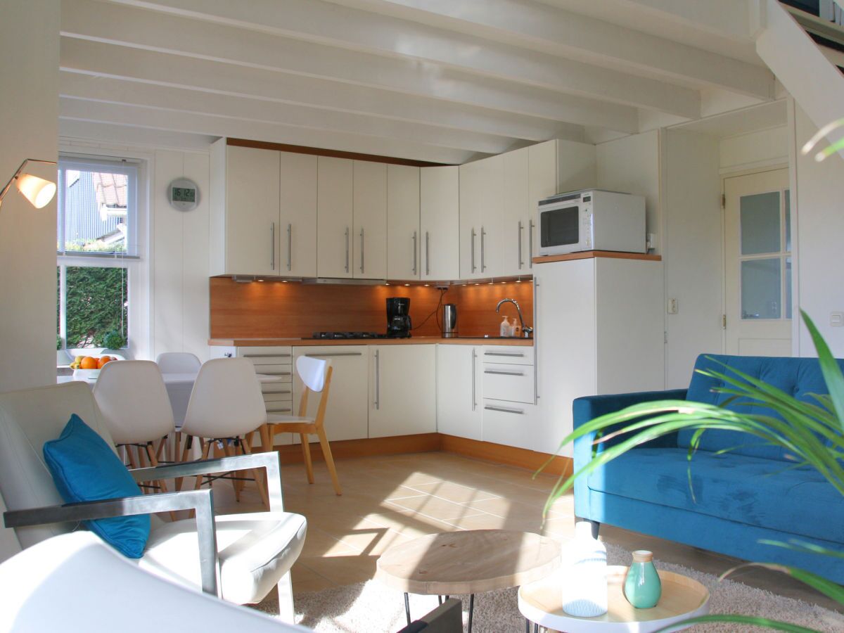 A modern kitchen with white cabinets, a microwave, and a coffee maker. There is a dining area with white chairs and a blue sofa.