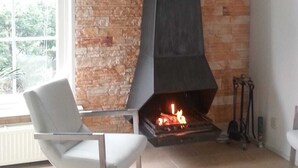 Uma sala de estar moderna com parede de pedra, lareira preta, cadeira branca e janela com vista para árvores.