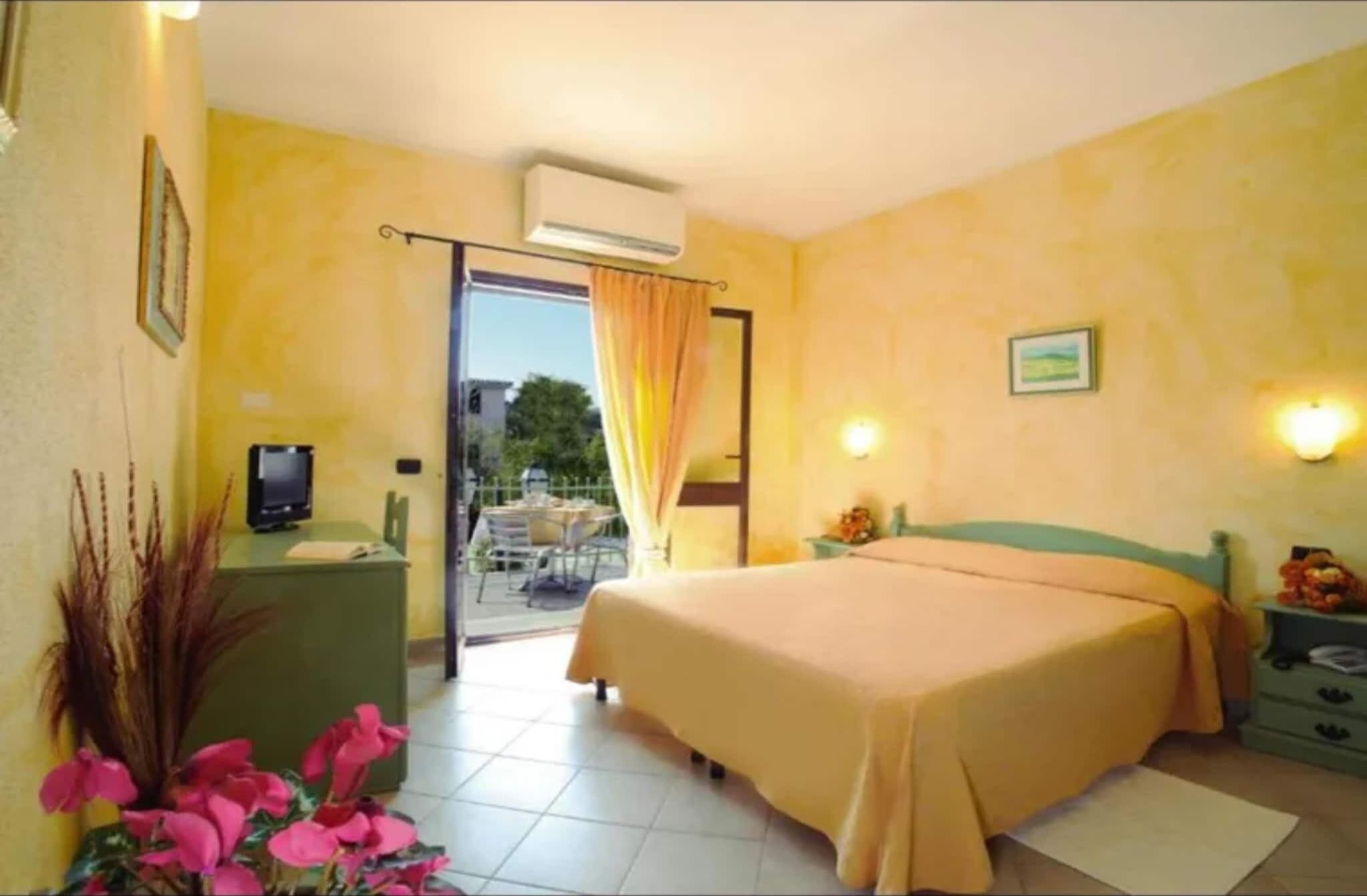 Hotelkamer met een bed, een bureau met een computer, een stoel, een raam met gordijnen en uitzicht op buiten.