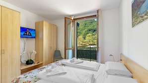 Habitació d'hotel amb dos llits, un televisor, un escriptori amb una planta i un balcó amb vista a vegetació.