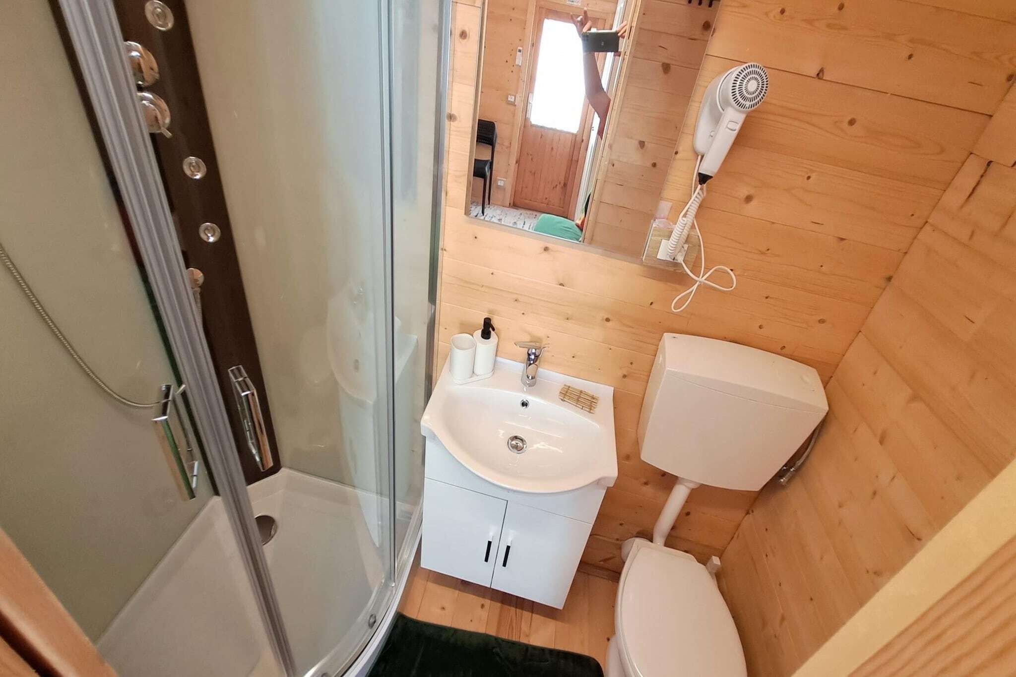 Un baño pequeño con ducha, lavamanos, inodoro y un secador de pelo fijado a la pared.