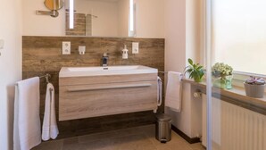A modern bathroom with a wooden vanity, a large mirror, and a window with plants. - Apartment in Grainau am Badersee (Graifenau)