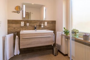 A modern bathroom with a wooden vanity, a large mirror, and a window with plants. - Apartment in Grainau am Badersee (Graifenau)