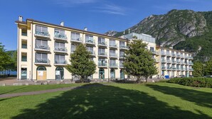 Ein mehrstöckiges Hotel mit Balkonen, einem grünen Innenhof und einer Bergkulisse.