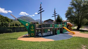 A playground with a slide and climbing structures, surrounded by grass and trees. - Appartement mit Seeblick auf den Luganersee (Porlezza)