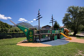 Ein Spielplatz mit Rutsche und Klettergerüsten, umgeben von Gras und Bäumen.