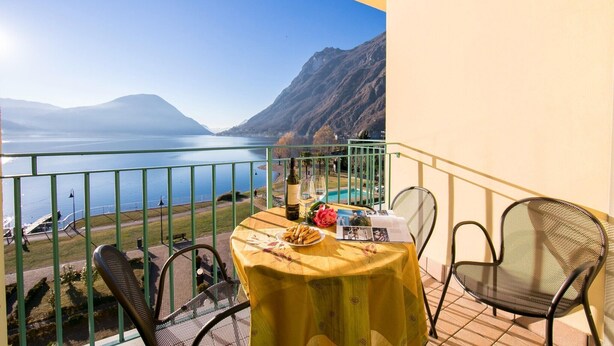 A balcony with a table set for two, overlooking a lake and mountains. - Appartement mit Seeblick auf den Luganersee (Porlezza)