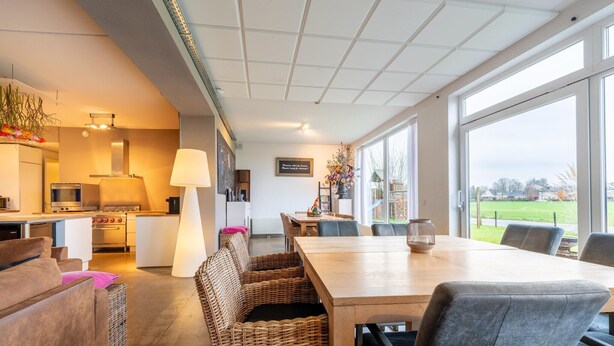 Een moderne keuken met witte apparaten, een eethoek met een houten tafel en rieten stoelen, en grote ramen met uitzicht op de omgeving.