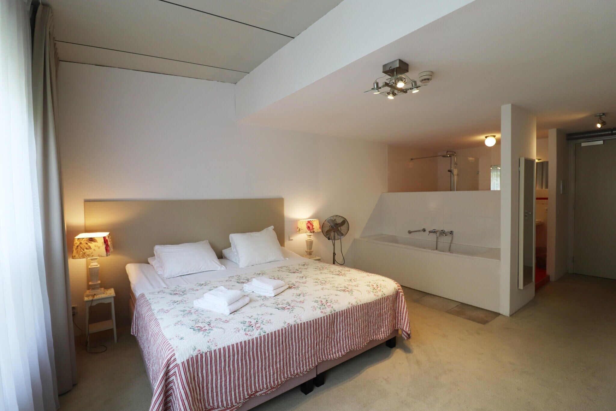 A bedroom with a bed, bedside table, lamp, and a large mirror.