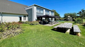 Een modern huis met twee verdiepingen, een verzorgd gazon, een terras en een klein zwembad.