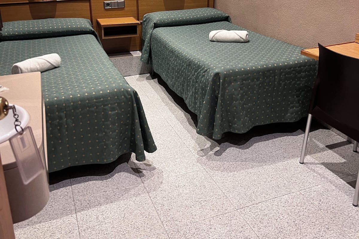 A hotel room with two single beds, a wooden nightstand, a small table, and a chair.