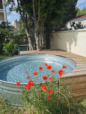 Ein Schwimmbecken mit Holzdeck, umgeben von Bäumen und Grün.