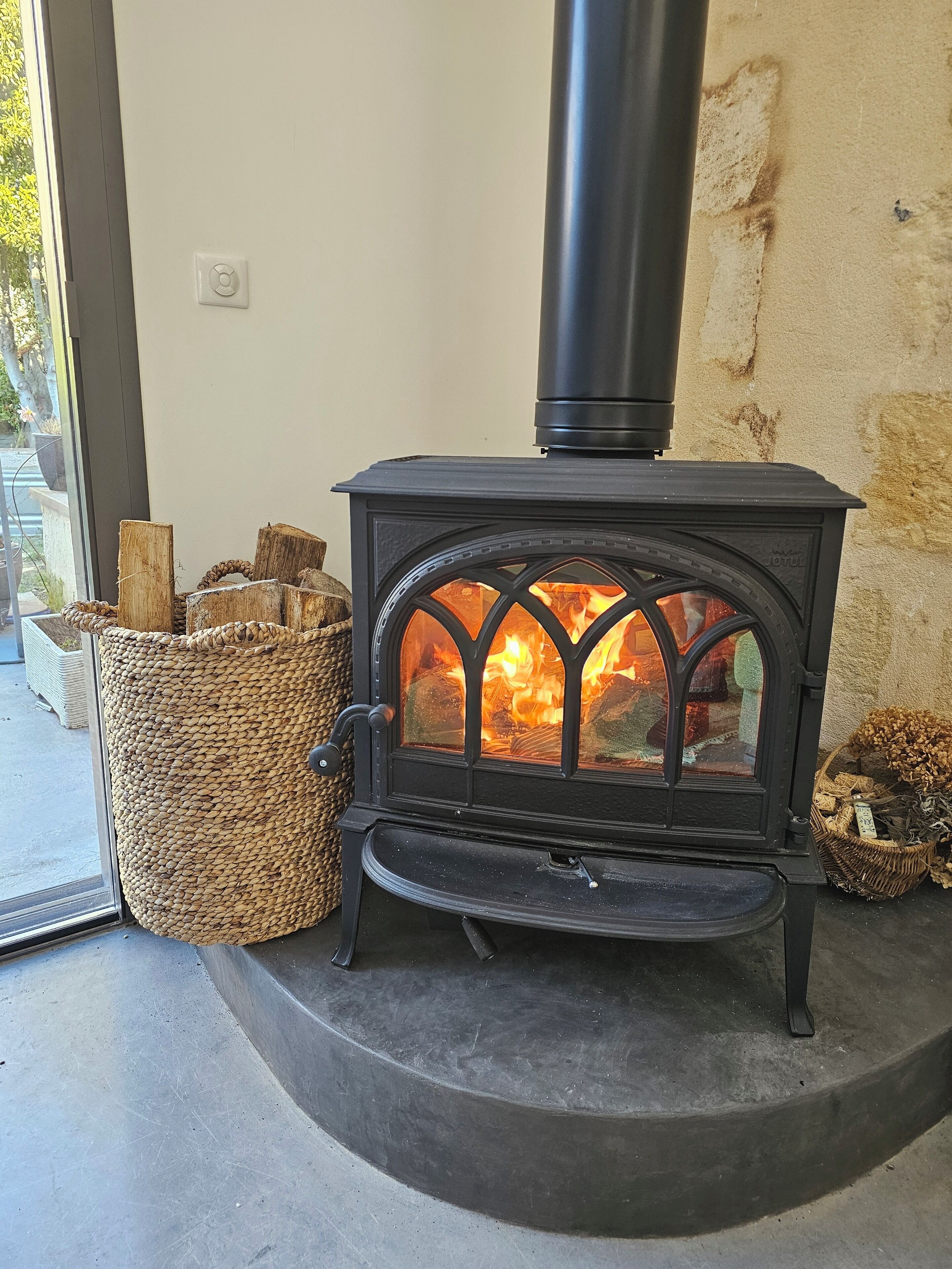 Ein Holzofen mit Glastür, Holzscheiten und einem Holzkorb.