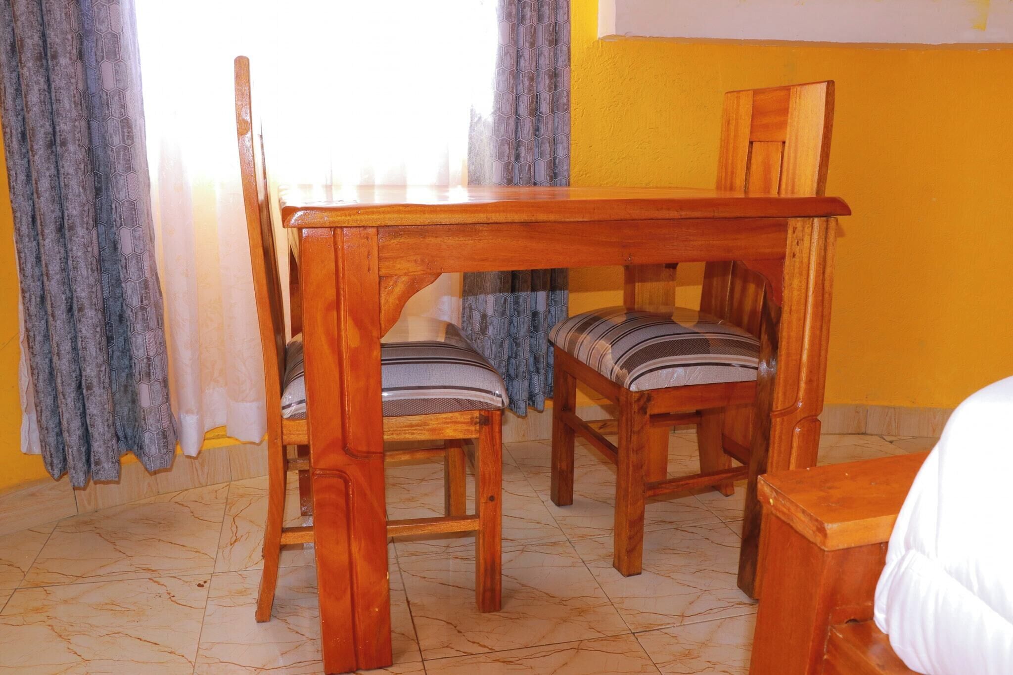 Una mesa de madera con dos sillas, una cama y una ventana con cortinas.