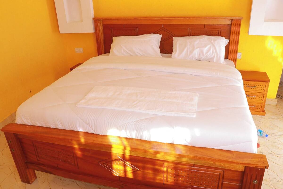A bed with white bedding, a wooden headboard, and a small wooden nightstand with a drawer.