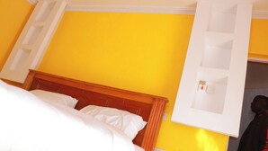 A hotel room with a bed, a wooden headboard, and a bright yellow wall.