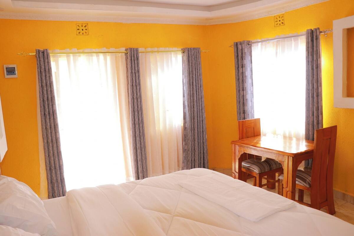 A hotel room with a bed, a wooden desk, and curtains.