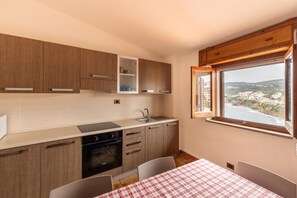 Eine kleine Küche mit Holzausstattung, einem Backofen und einem Fenster mit Blick auf die Küste.