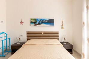 Un dormitorio con cama, mesita de noche, lámpara, una decoración de estrella de mar y un cuadro con escena de playa.