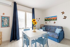 Una habitación con una mesa de comedor, sillas, un sofá, un jarrón con girasoles, un mapa y adhesivos murales de mariposas.
