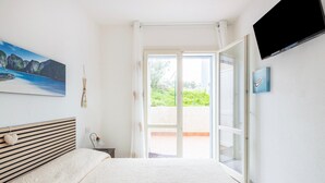 Una camera da letto con un letto, un quadro, una televisione e una porta scorrevole in vetro che dà su uno spazio all'aperto.