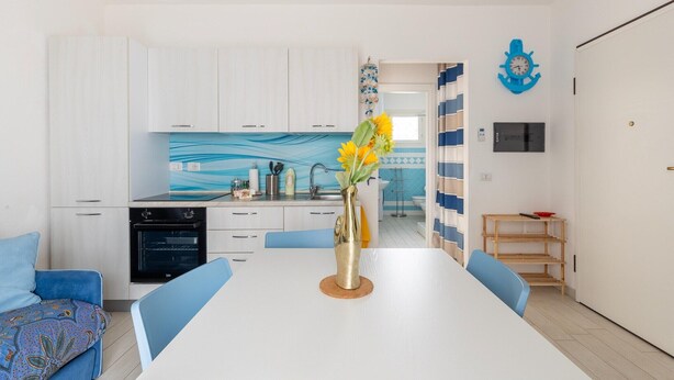 Una cucina moderna con mobili bianchi, uno schienale blu e un'area da pranzo con tavolo e sedie blu.