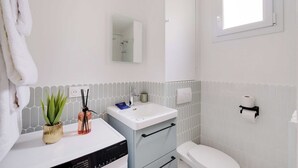 Et badeværelse med hvid vask, et spejl, et toilet, et håndklædestativ og et vindue.