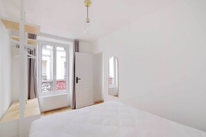 A bedroom with a bed, a wardrobe, a door leading to a balcony, and a hanging light fixture. - Charming apartment 1BR/3P - Oberkampf (Paris)
