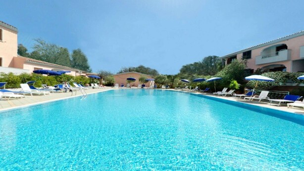 Ein klares, blaues Schwimmbecken mit Liegestühlen und Sonnenschirmen, umgeben von Gebäuden.